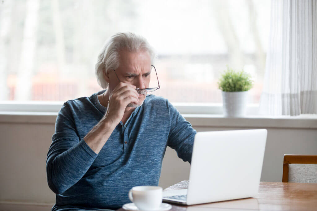 Shocked frustrated senior mature man taking off glasses to look at laptop reading shocking online news at home, stressed worried middle aged old male confused by bad email news or computer problem